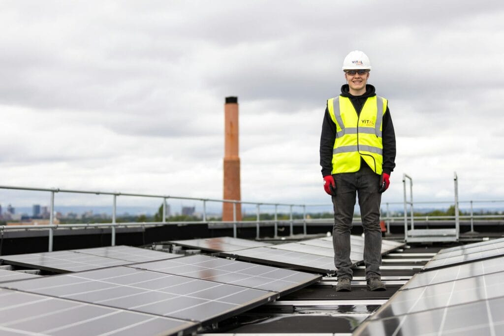 An engineer in a hard hat and safety vest inspects solar panels on a rooftop.